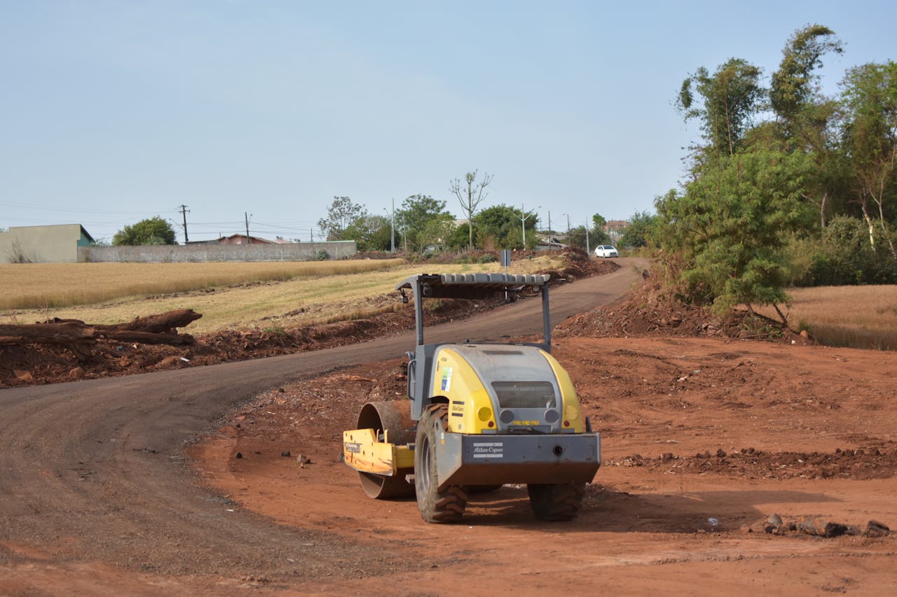services-02 Industrial scene with construction equipment on a dirt road surrounded by fields.
